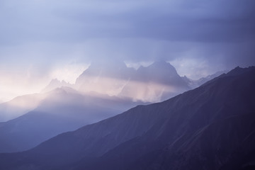 The blue mountains of Svaneti against the background of evening sky. The rays of setting sun illuminate snow-covered rocks of Georgia. Mountain tourism. Hike to the top.