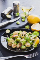 Roasted Brussel Sprouts with Parmesan cheese, lemon, Salt, Pepper on a black table.