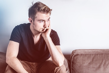 handsome businessman in black t-shirt and brown jean thinking on the brown sofa in living room with free copy space for your text