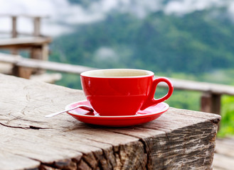 Red coffee cup with spoon on wooden table in the cafe at mountain viewpoint.