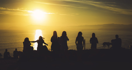 Group of young friends on background beach ocean sunrise, silhouette romantic people dances looking on rear view evening seascape, happy hipster enjoy sunset together, travel holidays vacation