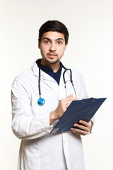 Fototapeta premium beautiful young doctor in a dressing gown with a stethoscope on a white background in the studio, records a medical history,