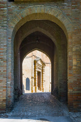 Fototapeta na wymiar Brick arch, secondary entrance of Saludecio, a little medieval town in the Montefeltro, in the Emilia Romagna region, between Rimini and Urbino. The door of a church appears in the background