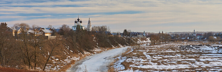 Early spring in Suzdal/City landscape of Suzdal. River, ice-bound, In the flood plain lies snow. On the slope of the hill, the snow melted and last year's grass is visible.Suzdal.Golden Ring of Russia