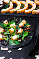Warm pumpkin salad with mixed leaf of arugula, chard, in on black slate plate on black background. Grilled pumpkin. Top view