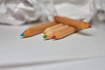 Packing of colored pencils on white paper on the main plane. Blurred crumpled sheets of paper in the background
