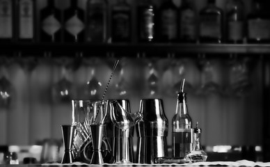 Set of bar accessories for making cocktails, located on the bar, behind is a shelving with liqueurs and strong alcohol.
