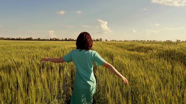 A young woman runs along the green field of wheat in a slow motion. Happy woman outdoors. Harvest. Wheat field in sunset.