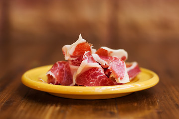 Spanish cuisine tapas food Jamon in a yellow plate. Beautiful appetite slices of raw pork meat. Close-up photo, soft focus, brown blurred abstract background