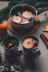 mulled wine in mugs and a saucepan on a concrete table with cones of fruit and cinnamon