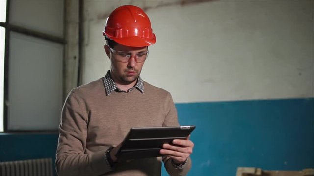 Young and ambitious architect uses tablet on site. He looks at the blueprints and watches for workers.