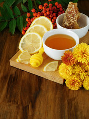 Liquid honey, lemon and rowan berries surrounded by flowers on a wooden board