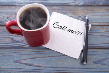 Inscription on a napkin Call me. and coffee in a red cup. Against a background of blue wood background.