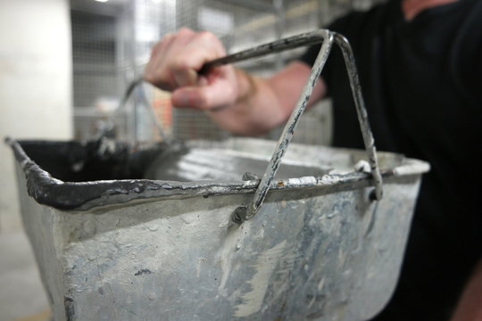 Man holding a dirty painter's bucket on top of a ladder