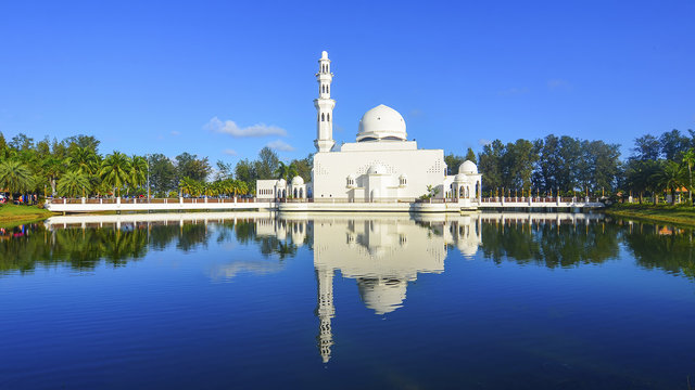 Mirror reflection of beautiful white floating mosque in a lake during blue sky.