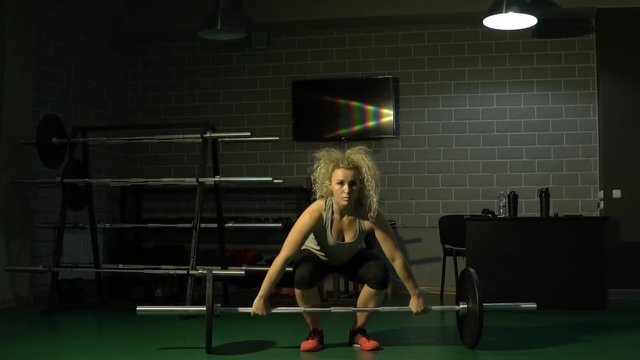A sporty beautiful girl lifts a heavy weight in the gym. Slow motion