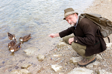 man in his 50s sitting by the water and feeding ducks