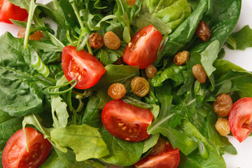 Fresh salad with greens, tomatoes and raisins, closeup.