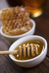 Honey dripping from a wooden honey dipper in a jar on wooden background