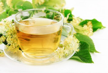Glass cup of herbal linden tea with fresh green lime tree leaves and yellow blossom. Tasty and healthy drink. 