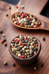 Peppercorns whole in rustic bowl on wooden board. Macro shot.