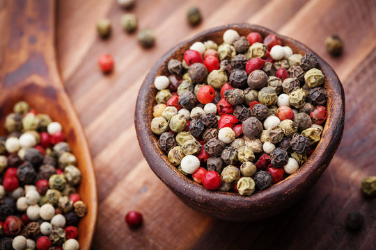 Mixed colorful peppercorns in rustic bowl on wooden table. Macro shot.