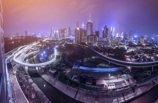 Panorama view of Kuala Lumpur city skyline during blue hour with busy traffic on highway.