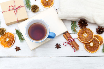 A cup of hot tea is on the book, and around the Christmas decorations on a wooden background. Flat lay