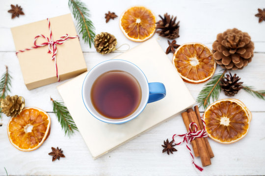 A cup of tea is on a book, and around the Christmas decorations on a wooden background. Top view