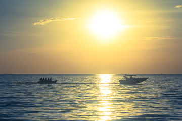 Silhouette of people playing banana boat on the sea with beautiful view of sunset light in the background at Chao Lao Beach, Chanthaburi Province, Thailand.