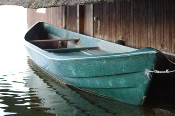 Green boat under the roof of a wooden house in a lake