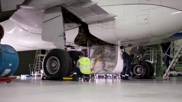 Inspection and preparing the aircraft before take off. Maintenance of passenger aircraft chassis at hangar before flight. Airport workers mechanic