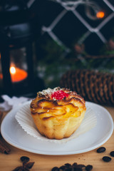 A small cake on the plate in the Christmas atmosphere with the candle lights and cone