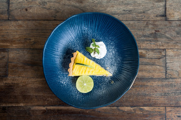 Top view image of a yellow lemon curd cake in blue ceramic plate on wooden table