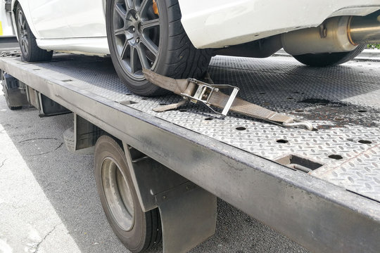 Car tire secured with safety belt on flatbed tow truck
