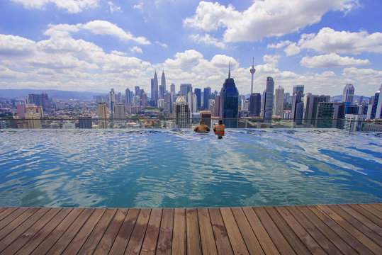 Unidentified Businessman And Traveller Swimming In Infinity Pool With Kuala Lumpur City Skyline And Dramatic Cloud Formation At Background.