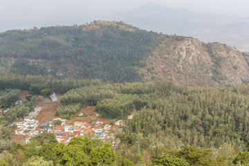 Wide angle view of a houses in a village developed in between the mountain. Wide view of mountain landscape with lots of tree.