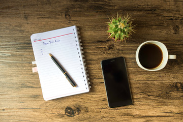 Top view new year goals list with notebook, cup of coffee on wooden desk