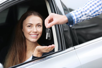 Young woman receiving key while sitting on driver's seat of car