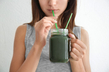 Woman drinking spirulina cocktail on light background
