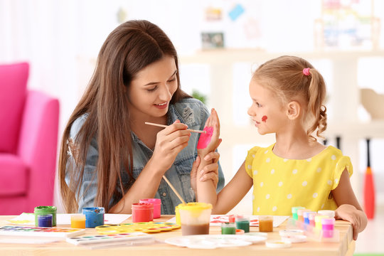 Cute girl with mother painting at table indoors