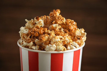 Cup with tasty caramel popcorn on blurred background, closeup