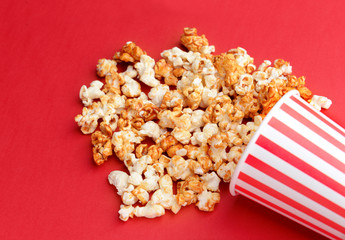 Overturned cup with tasty caramel popcorn on color background