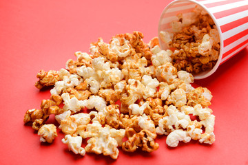 Overturned cup with tasty caramel popcorn on color background
