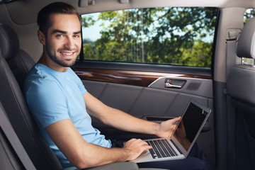 Young man with laptop on backseat of car