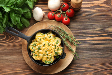 Board with potato casserole in pan and vegetables on wooden table