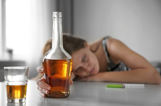 Bottle and glass of alcohol with woman on background