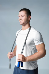 Young man with jumping rope on light background