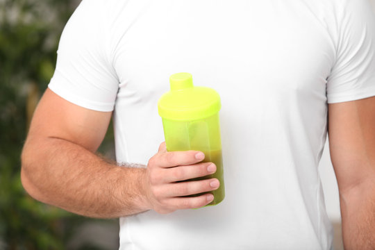 Young man holding bottle with protein shake, closeup