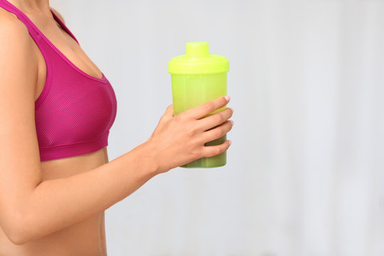 Young woman holding bottle with protein shake on blurred background